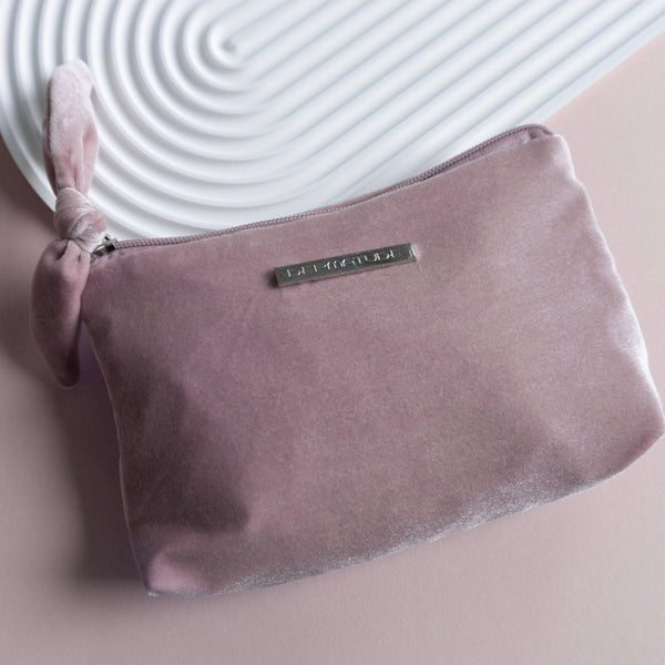 A pink velvet clutch that says DERMATUDE.